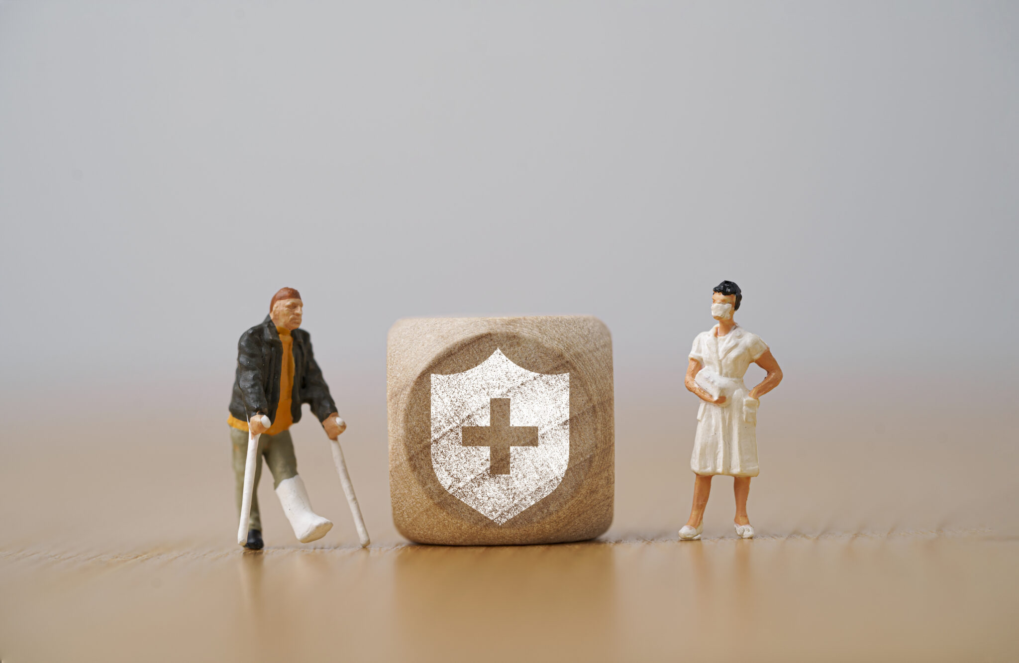 Miniature figure  man with a broken leg uses a crutch standing beside with nurse and insurance sign for healthcare assurance claim and medical concept.