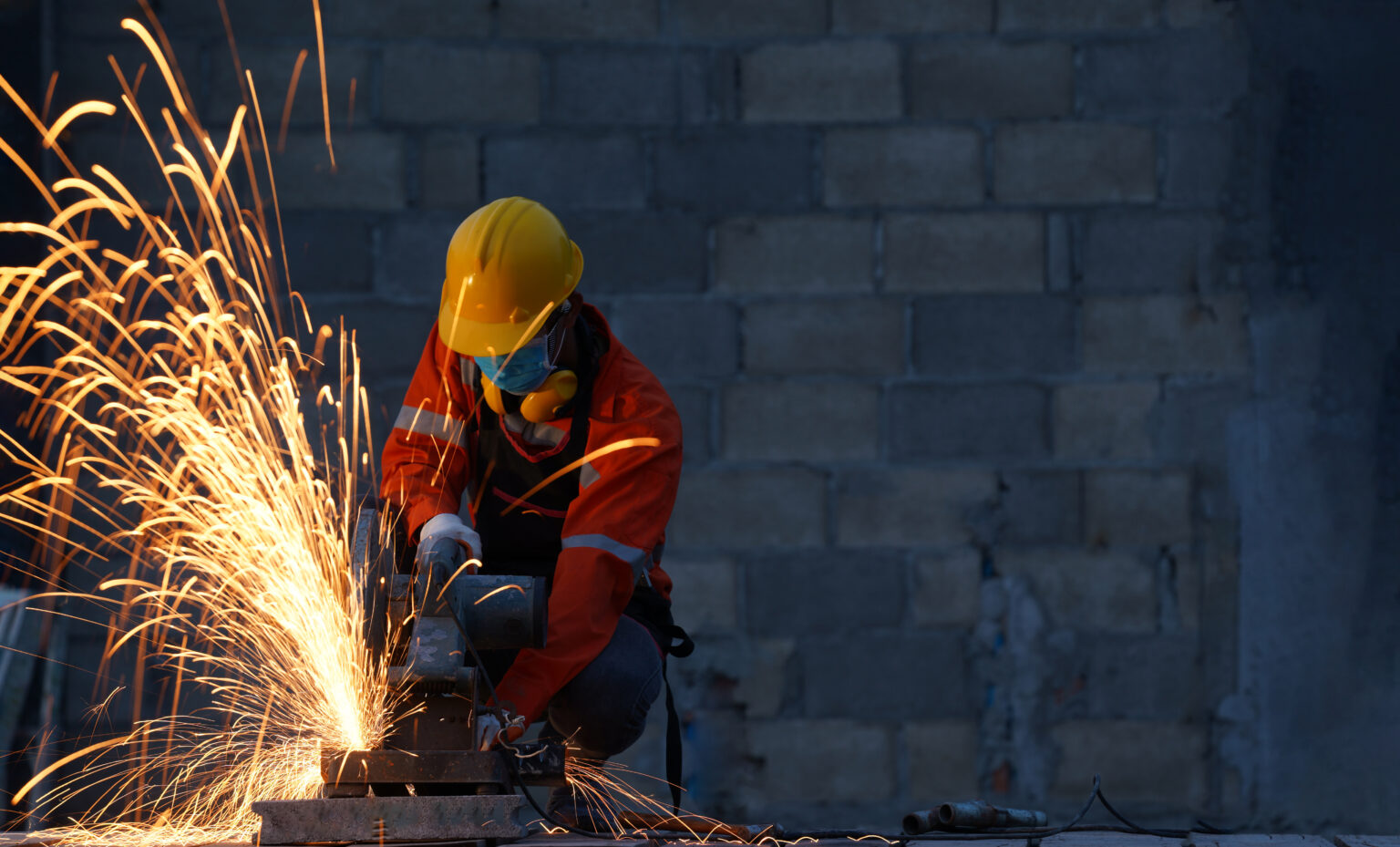 Worker wearing protective mask to Protect Against Covid-19,Sparks from sawing metal at a construction site,Worker using grinder steel and have throwing sparks.